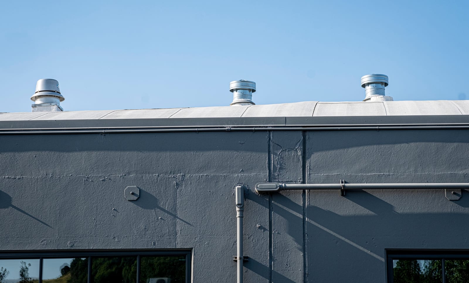 Low-slope commercial roof edge with ventilation penetrations and visible wall transition
